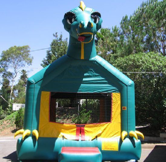 Teal dragon-themed bounce house with yellow accents in a sunny outdoor yard