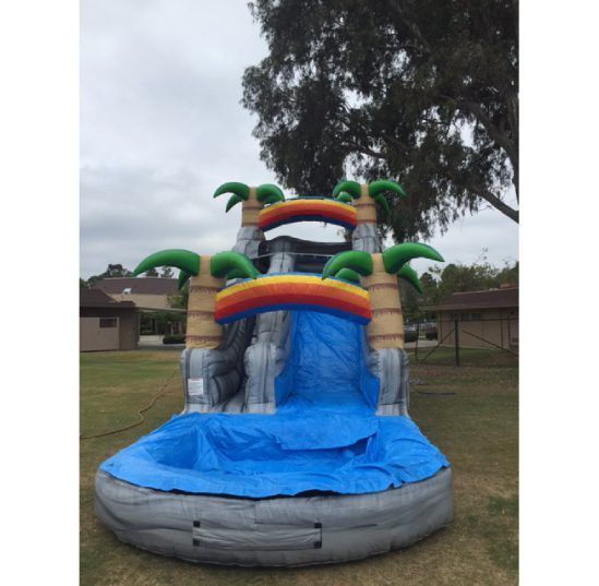 Colorful inflatable water slide with blue landing pool, shaped like a tropical castle outdoors.