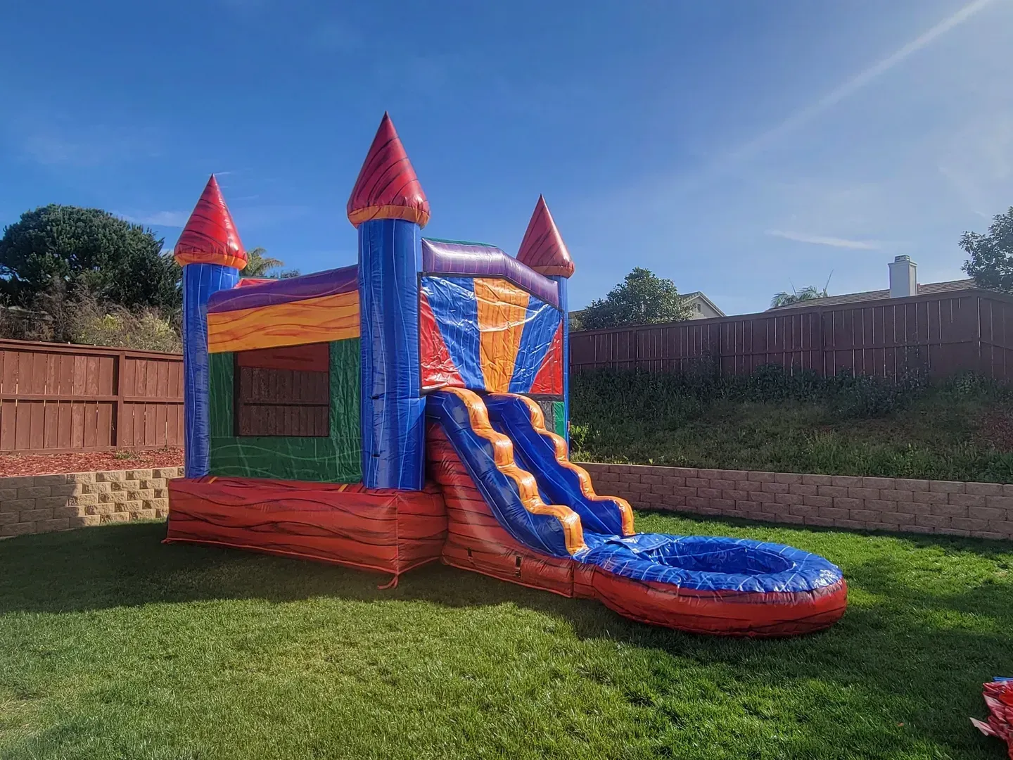 Colorful inflatable bounce house and slide on a grassy backyard under a sunny sky