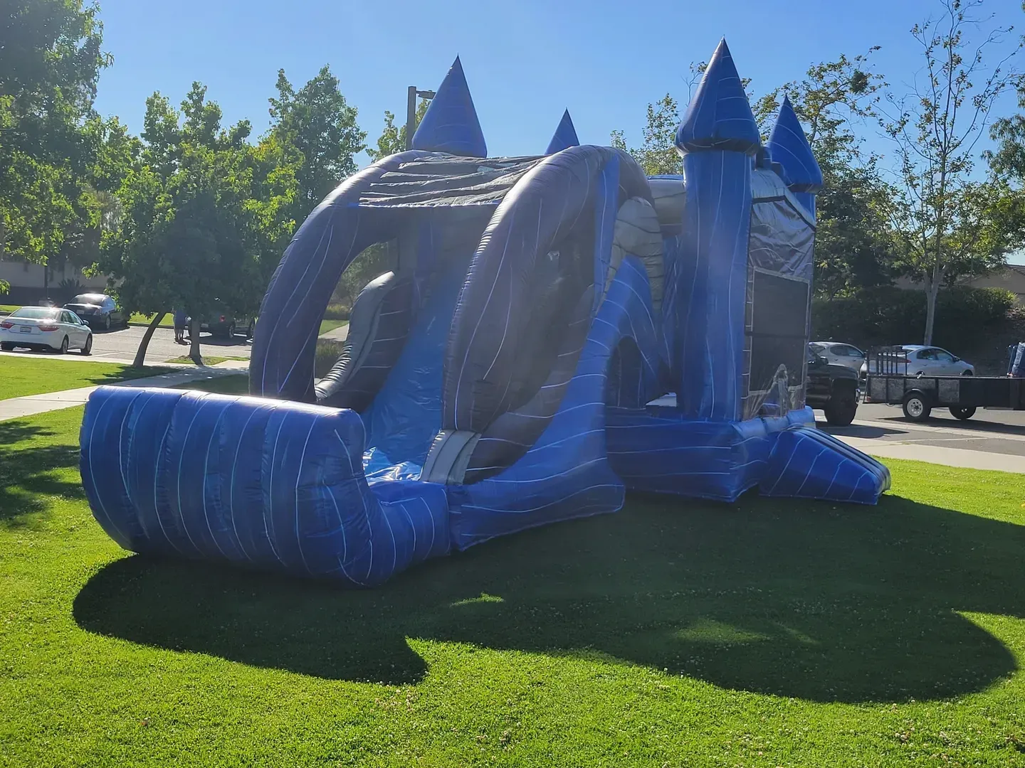 Blue inflatable bounce house with slide and castle turrets on a grassy lawn in sunlight