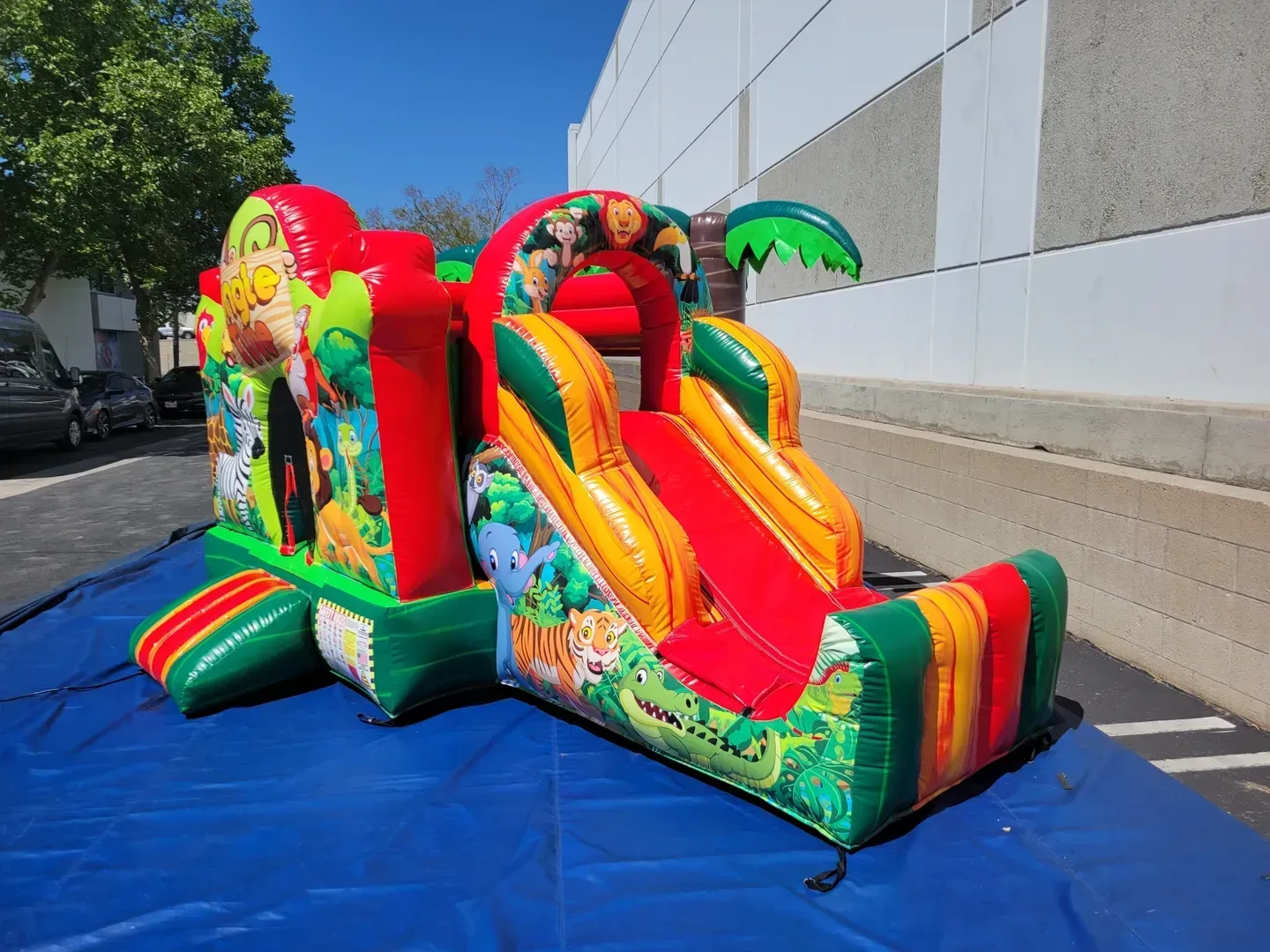 Colorful inflatable slide and bounce house set up on a blue tarp outdoors beside a building