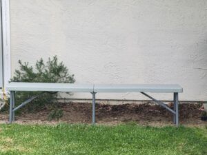 Metal bench beside a beige wall with shrubs and grass nearby