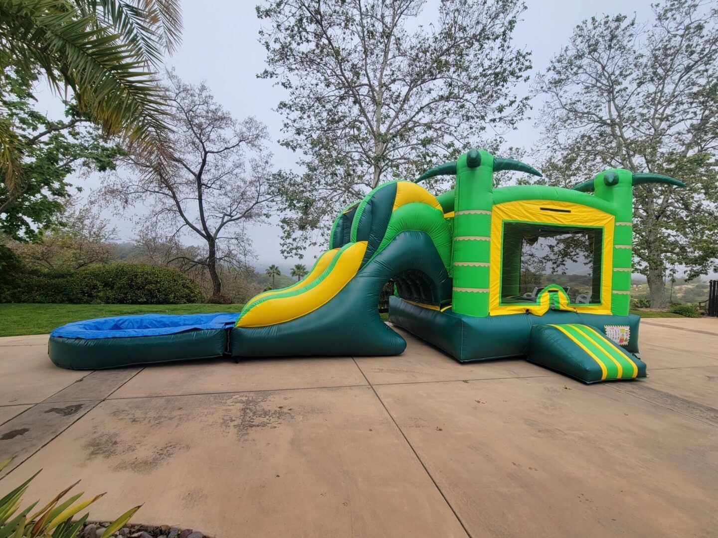 Green inflatable bounce house with slide and netted entrance on a concrete pad outdoors