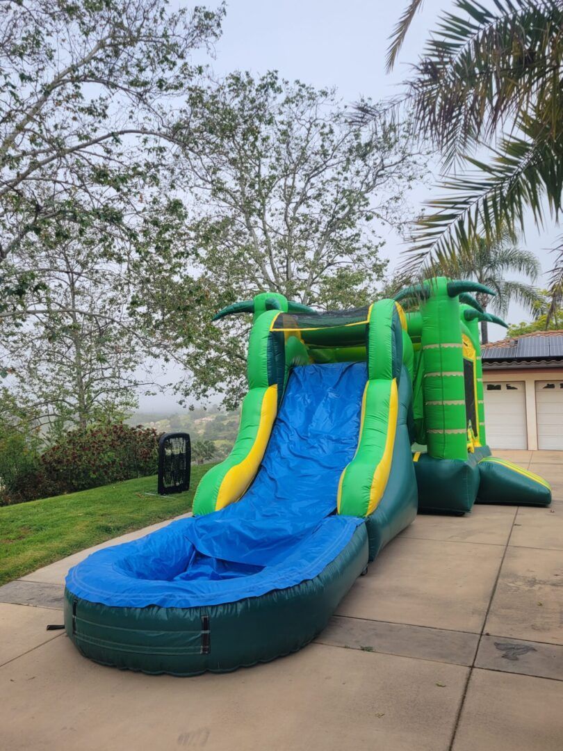 Green and blue inflatable waterslide on a paved path in a grassy park area