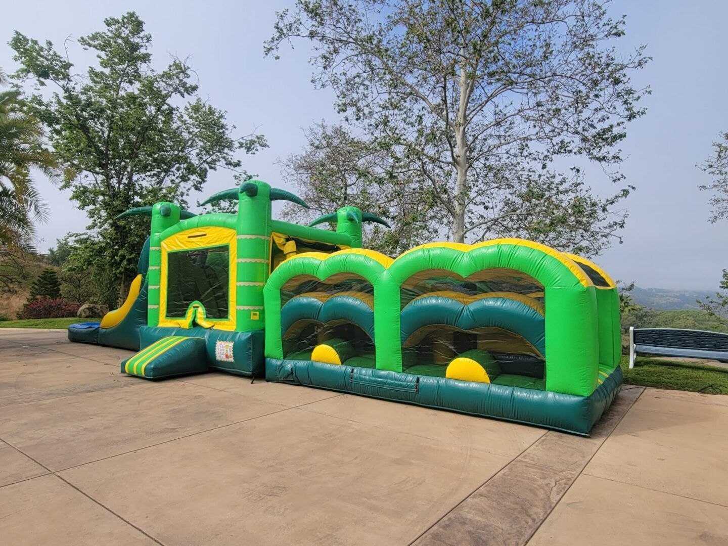 Green inflatable obstacle course with yellow accents on a concrete driveway outdoors