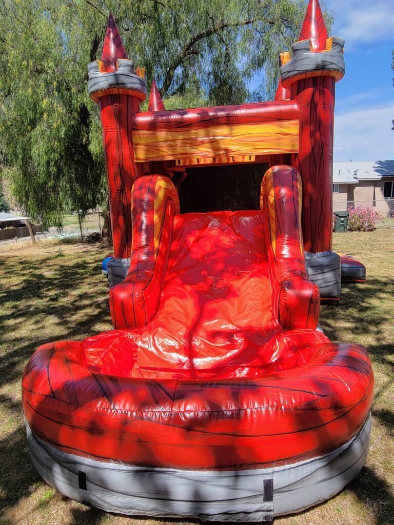Red inflatable castle bounce house with two towers and a slide outdoors in a yard