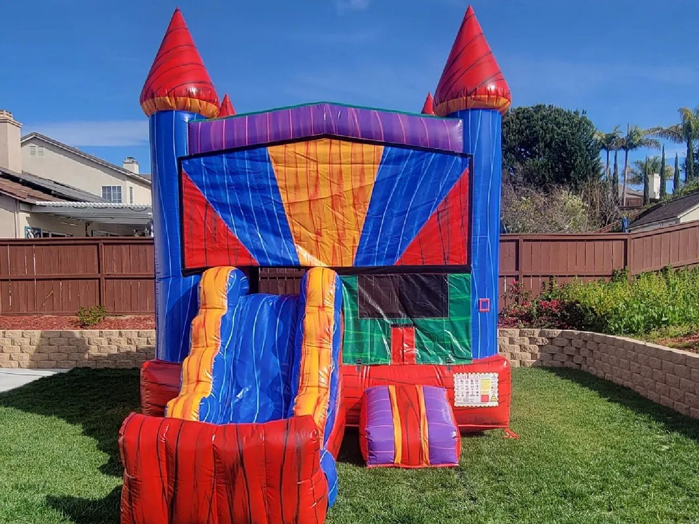Colorful inflatable bounce house with slide in a sunny backyard, red and blue with castle towers