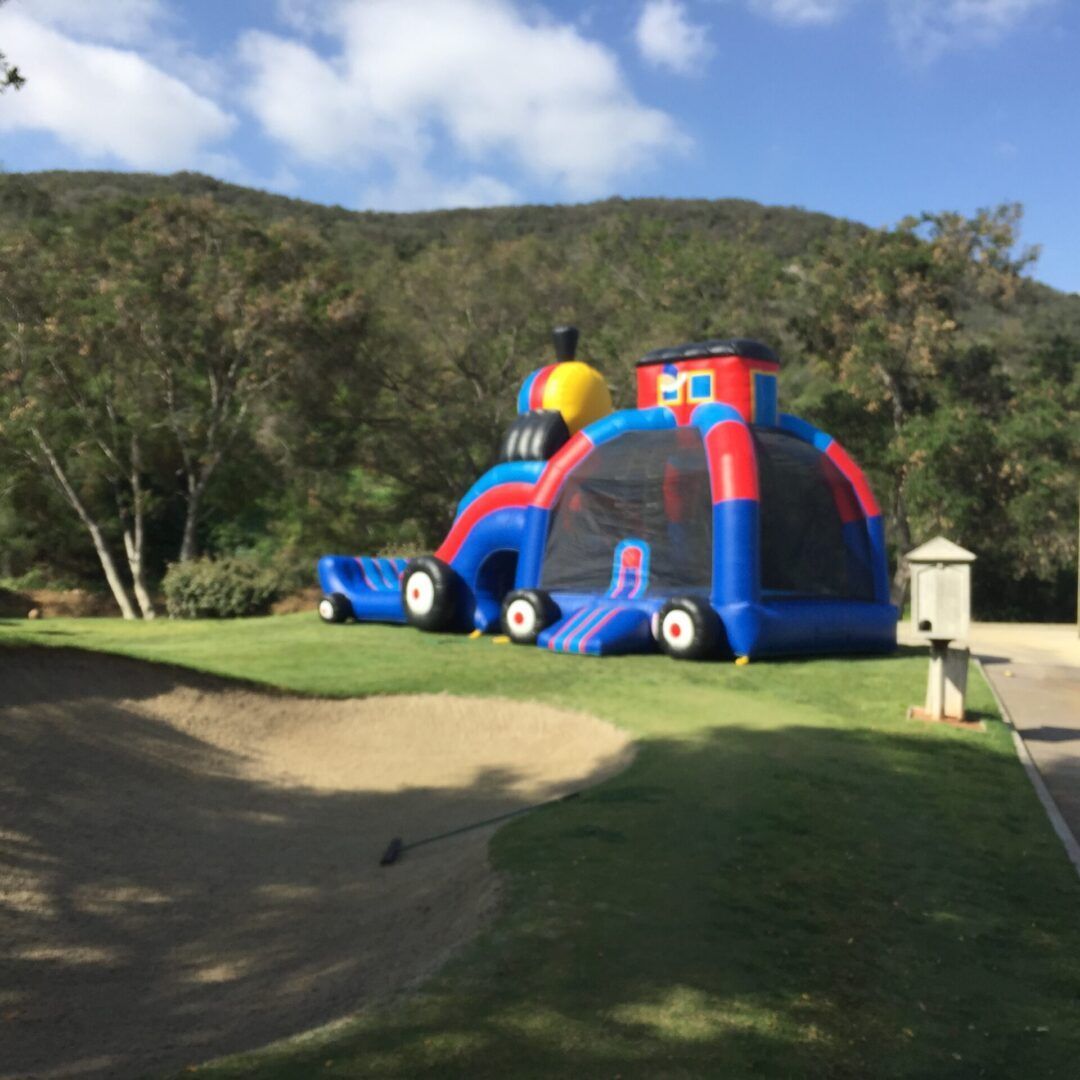 Inflatable obstacle course with blue and red arches on a grassy field beside a dirt path
