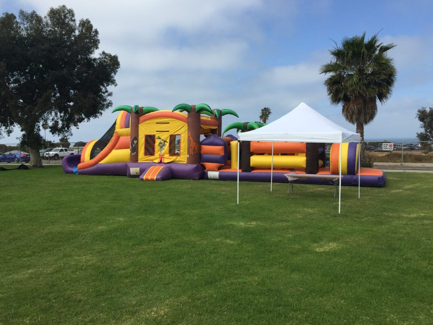 Colorful inflatable bounce house on a grassy field beside a white canopy tent under a cloudy sky
