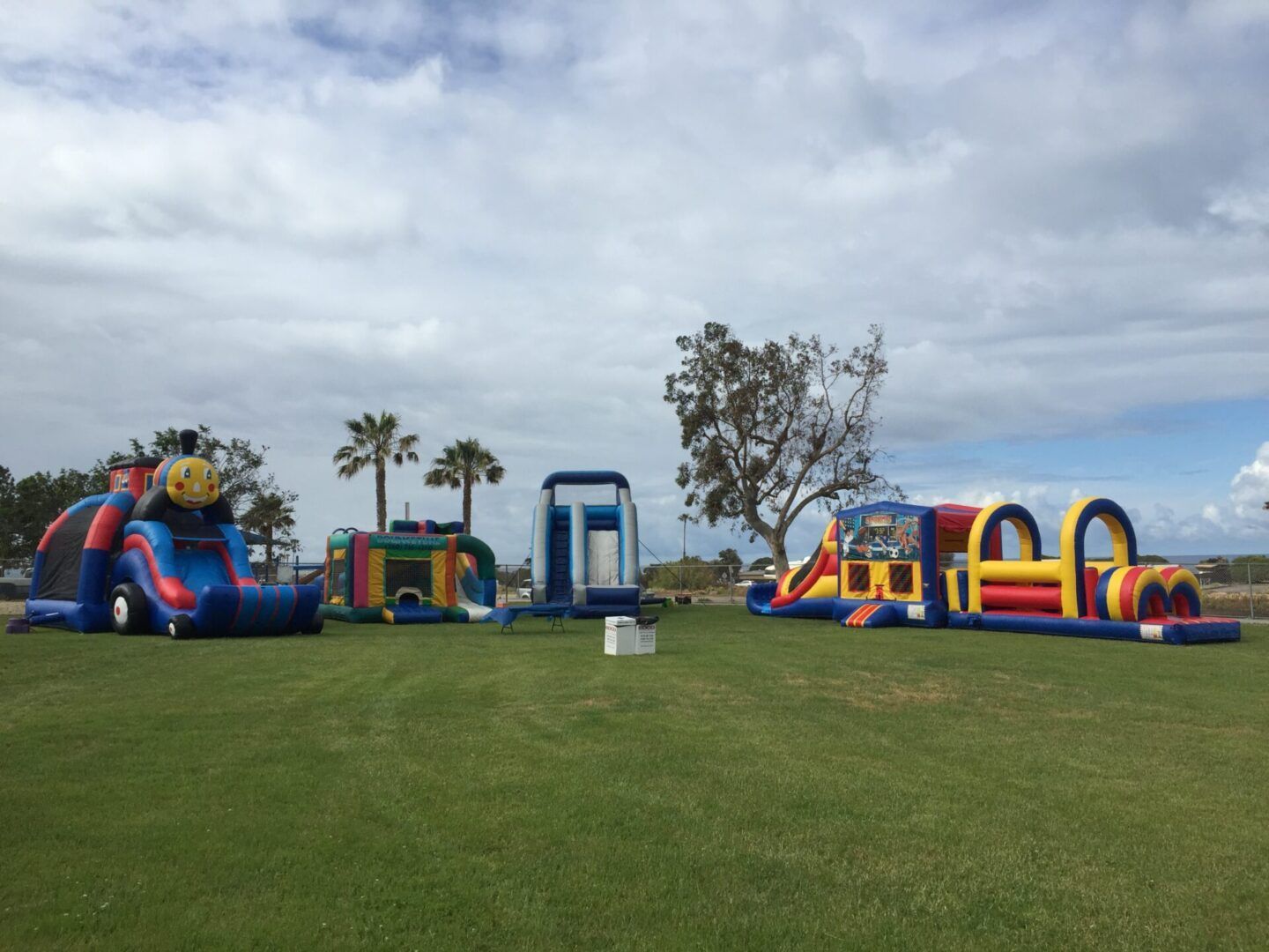 Colorful inflatable obstacle courses on a grassy field under a cloudy sky.