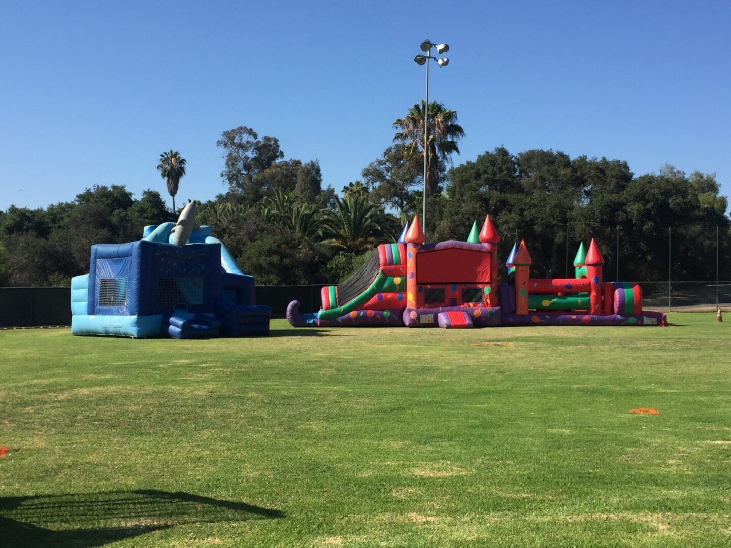 Inflatable bounce house and slide play area on a grassy field under a clear sky