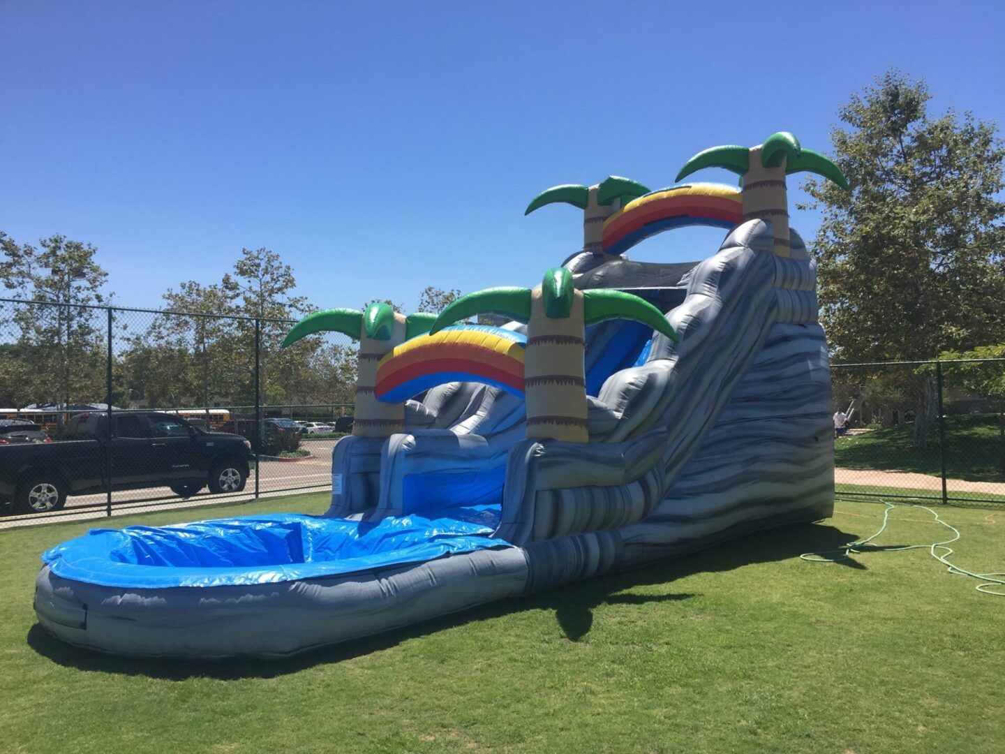 Large blue inflatable waterslide with rainbow arches and a splash pool on a grassy field.