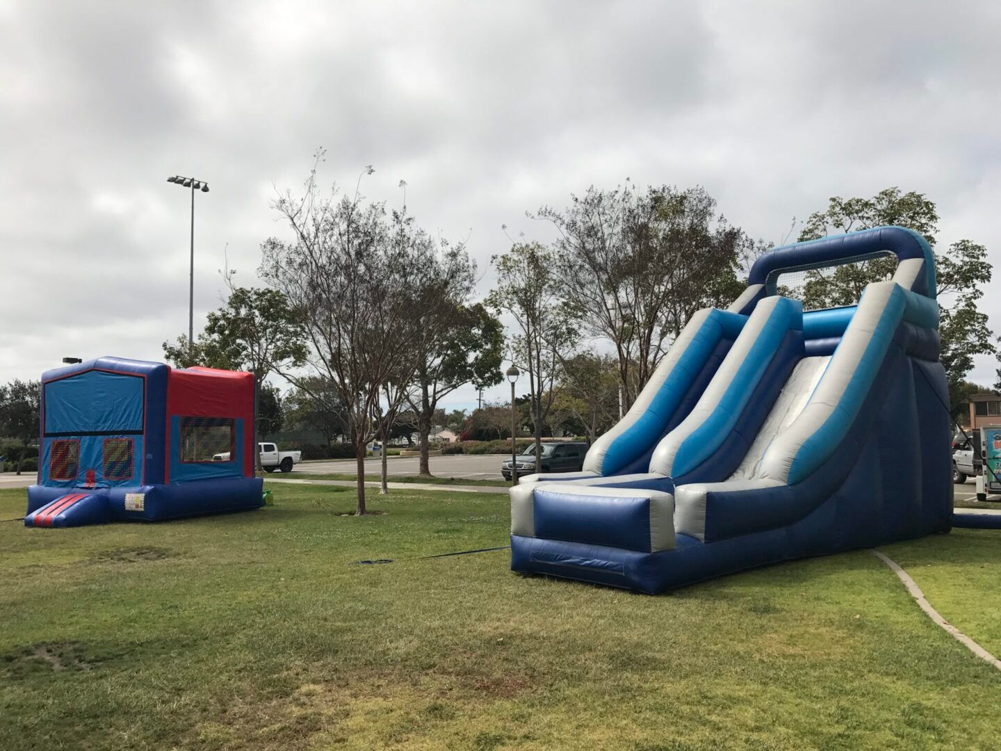 Inflatable bounce house and dual slide on a grassy park field under cloudy skies