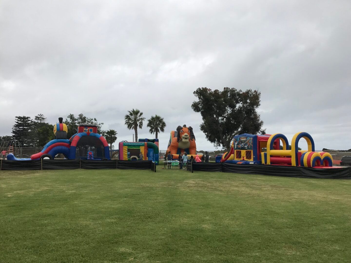 Colorful inflatable bounce houses on a grassy field under a cloudy sky, with a few people nearby.