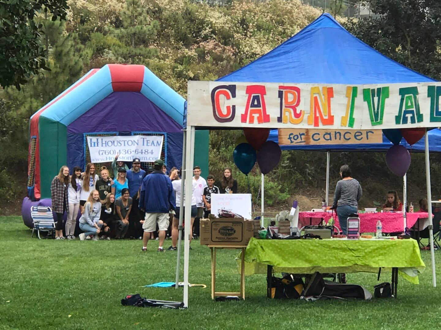 Outdoor cancer fundraiser booths with people near a blue tent and a colorful 