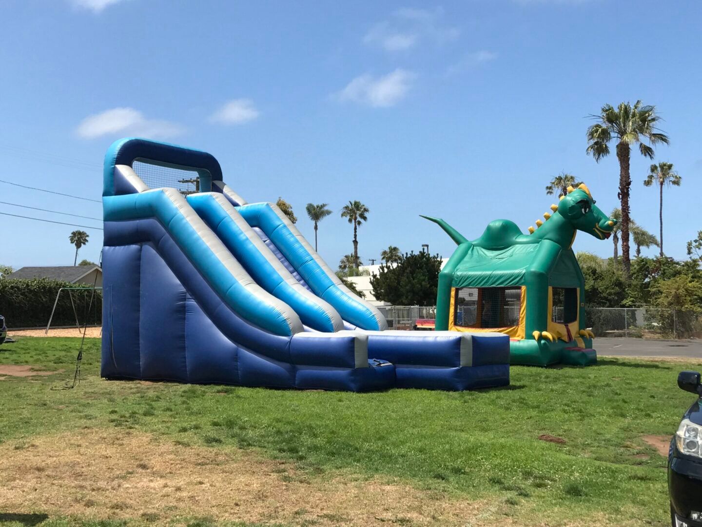 Blue inflatable slides and a green bounce house on a grassy field under a sunny sky
