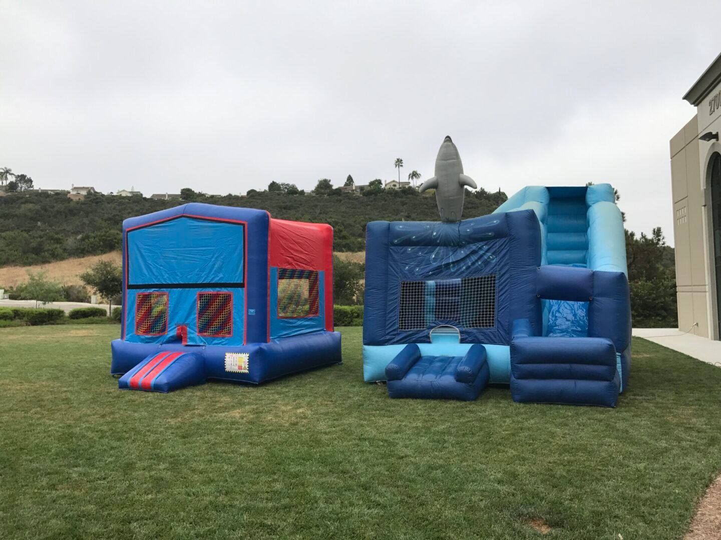 Blue inflatable bounce houses on a grassy lawn with hills in the background
