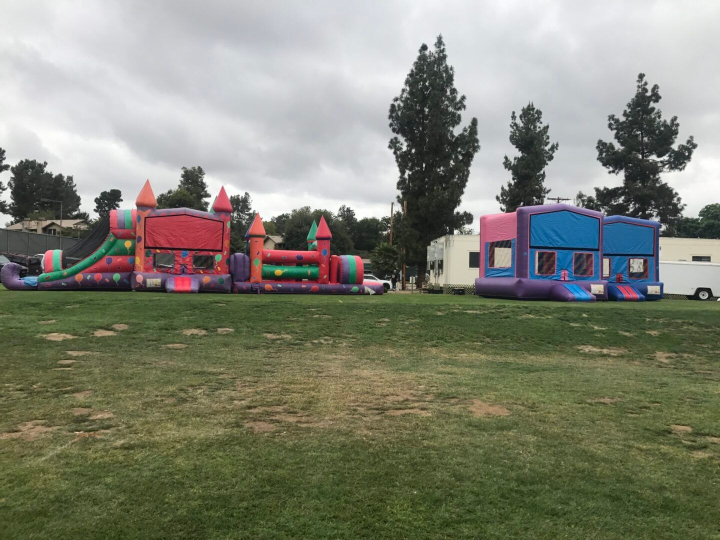 Colorful inflatable bounce houses on a grassy field under a cloudy sky