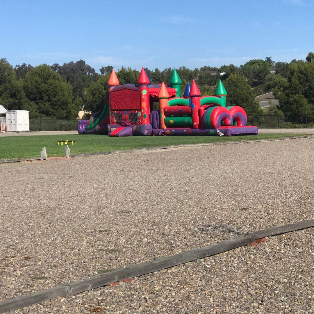 Colorful inflatable bounce house on a grassy field beside a gravel lot under a clear sky.
