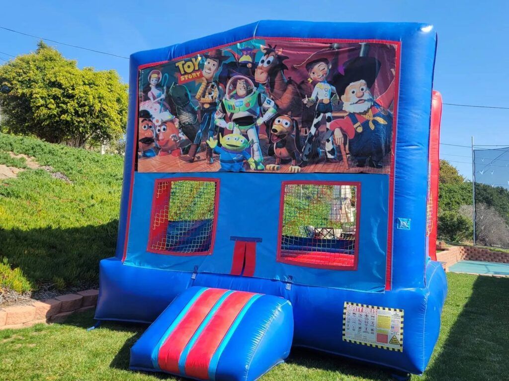 Blue inflatable bounce house with colorful cartoon banner and red windows on a grassy field