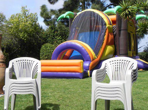 Inflatable bouncy castle in a grassy yard with two white plastic chairs in the foreground