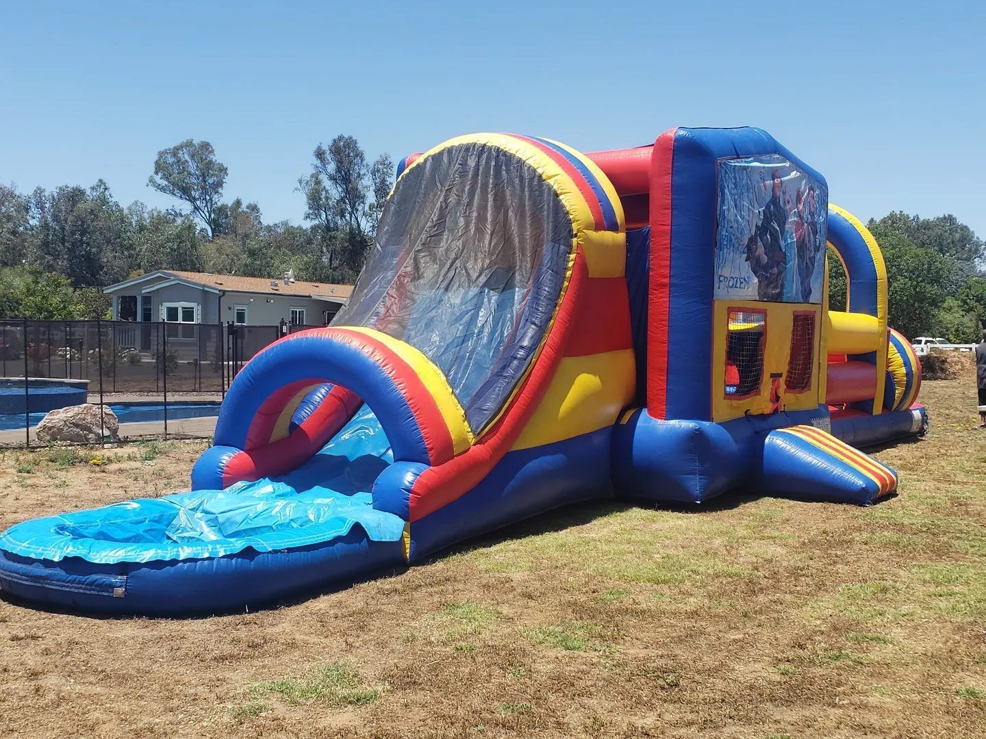 Colorful inflatable water slide on dry grass outdoors, with blue and red sides and a small pool at the bottom