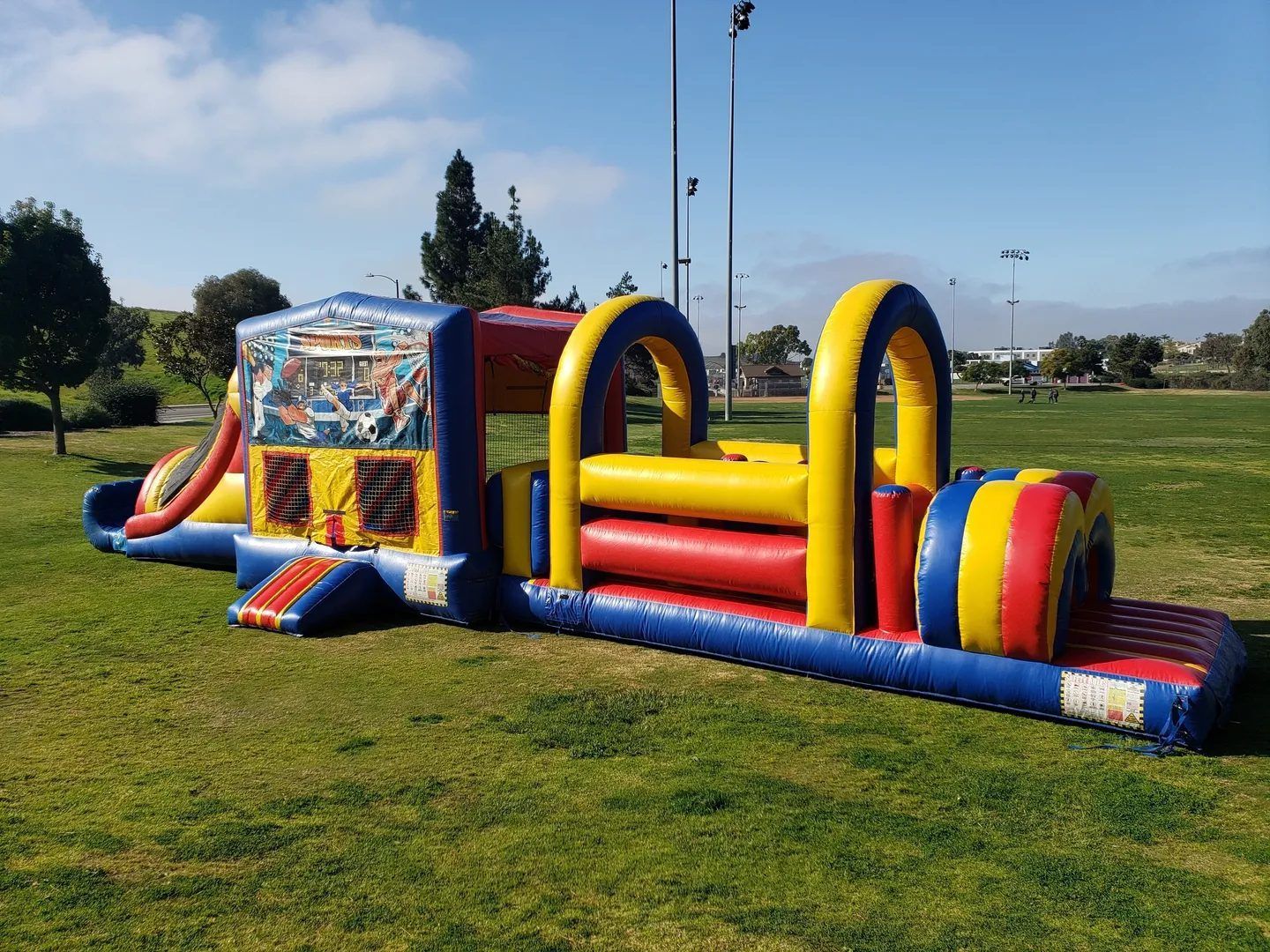 Colorful inflatable obstacle course on a grassy field under a clear blue sky.