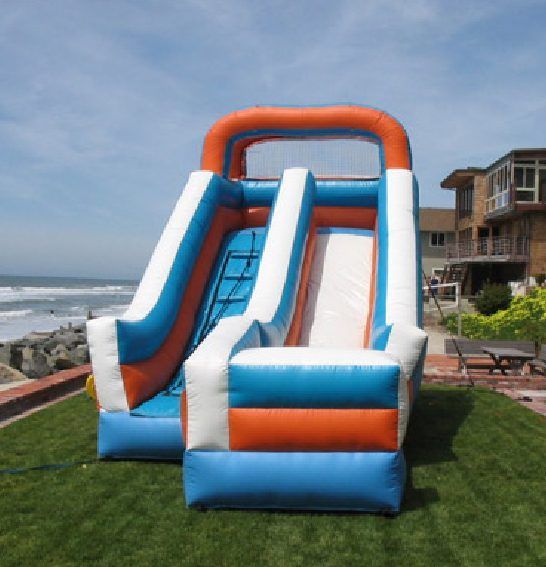 Inflatable blue, white, and orange slide on grass by the ocean near a house