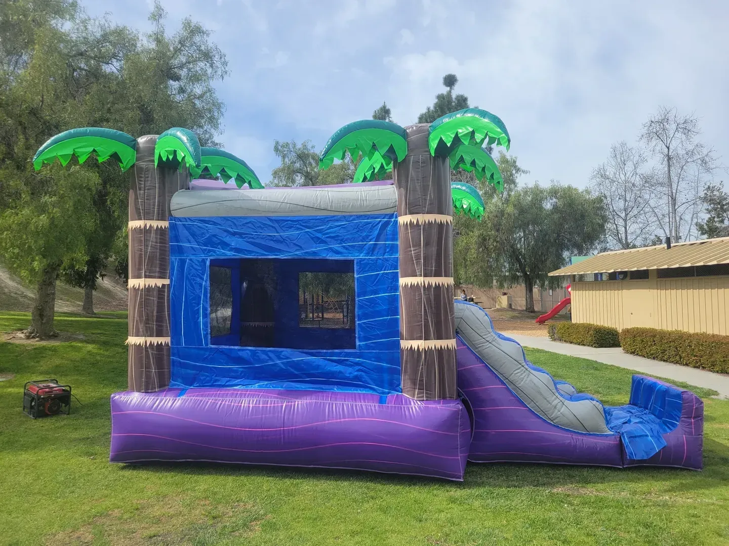 Purple and blue inflatable bounce house with palm tree decorations on a grassy field