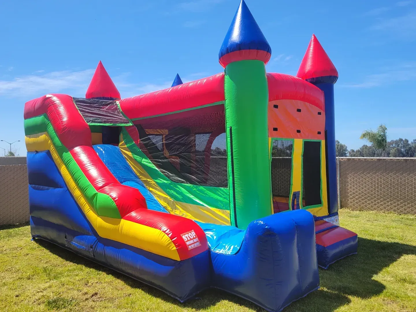 Colorful inflatable bounce house with slide and mesh sides in a sunny backyard