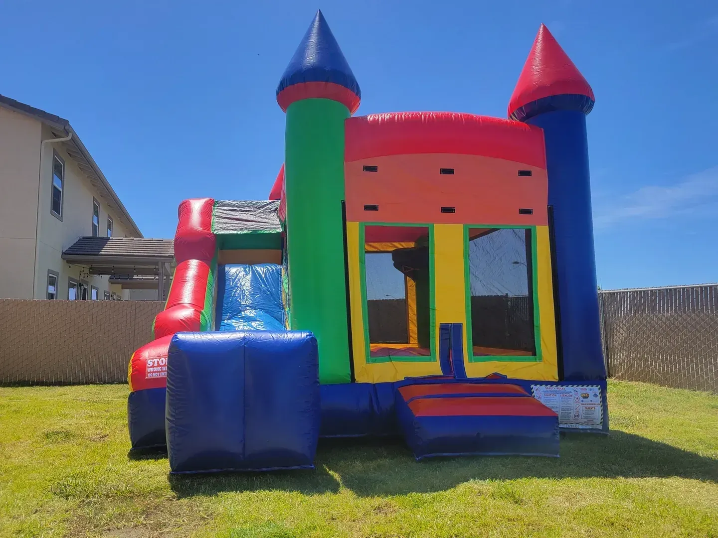 Colorful inflatable bounce house with slide on a grassy backyard under a clear blue sky