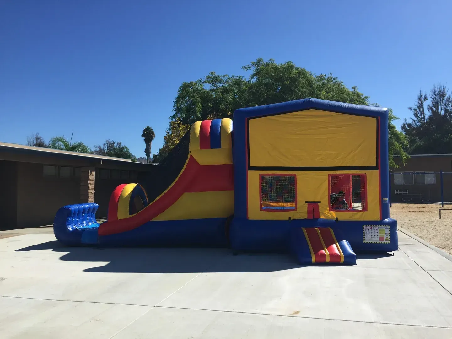 Colorful inflatable bounce house with slide and small steps in a sunny outdoor lot