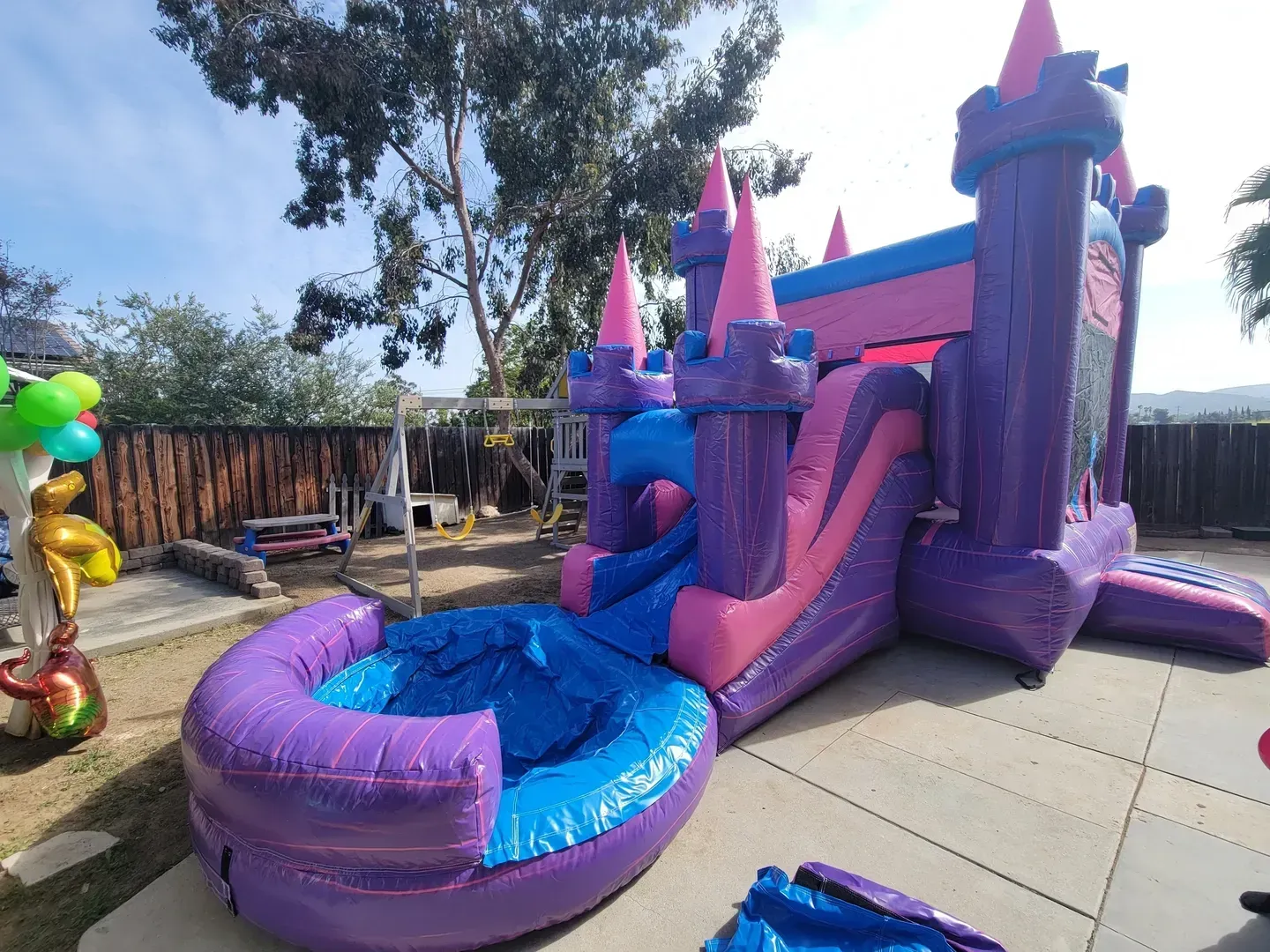Purple and blue inflatable slide with splash pool in a sunny backyard