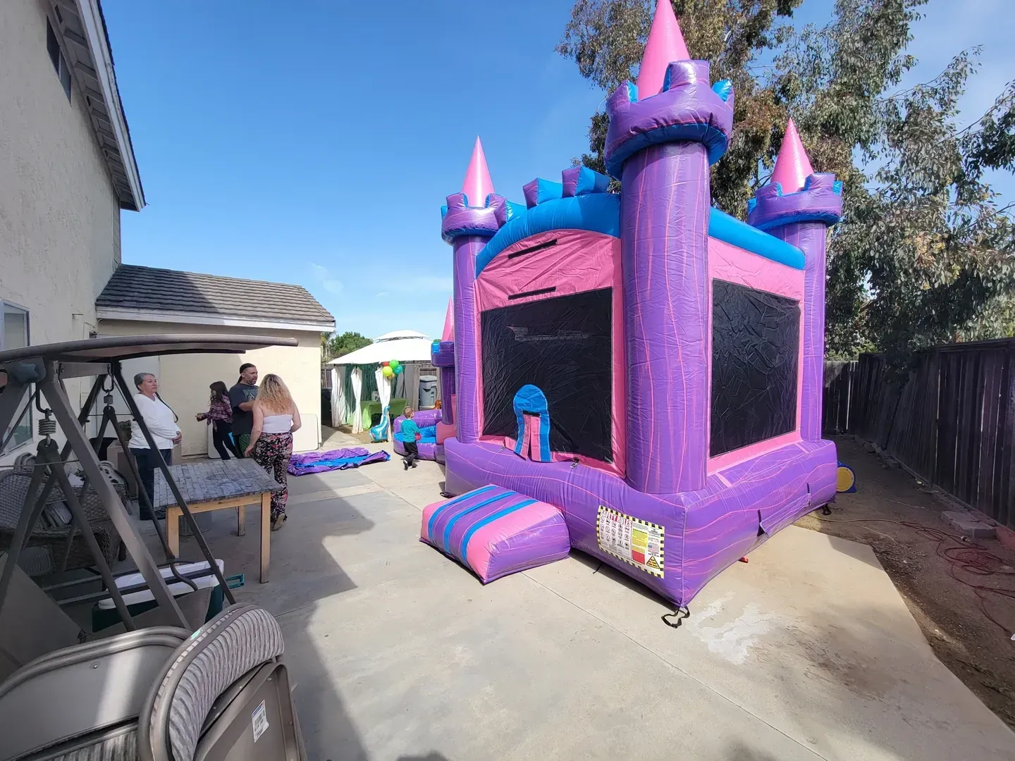 Purple inflatable castle bounce house with pink towers in a sunny outdoor courtyard