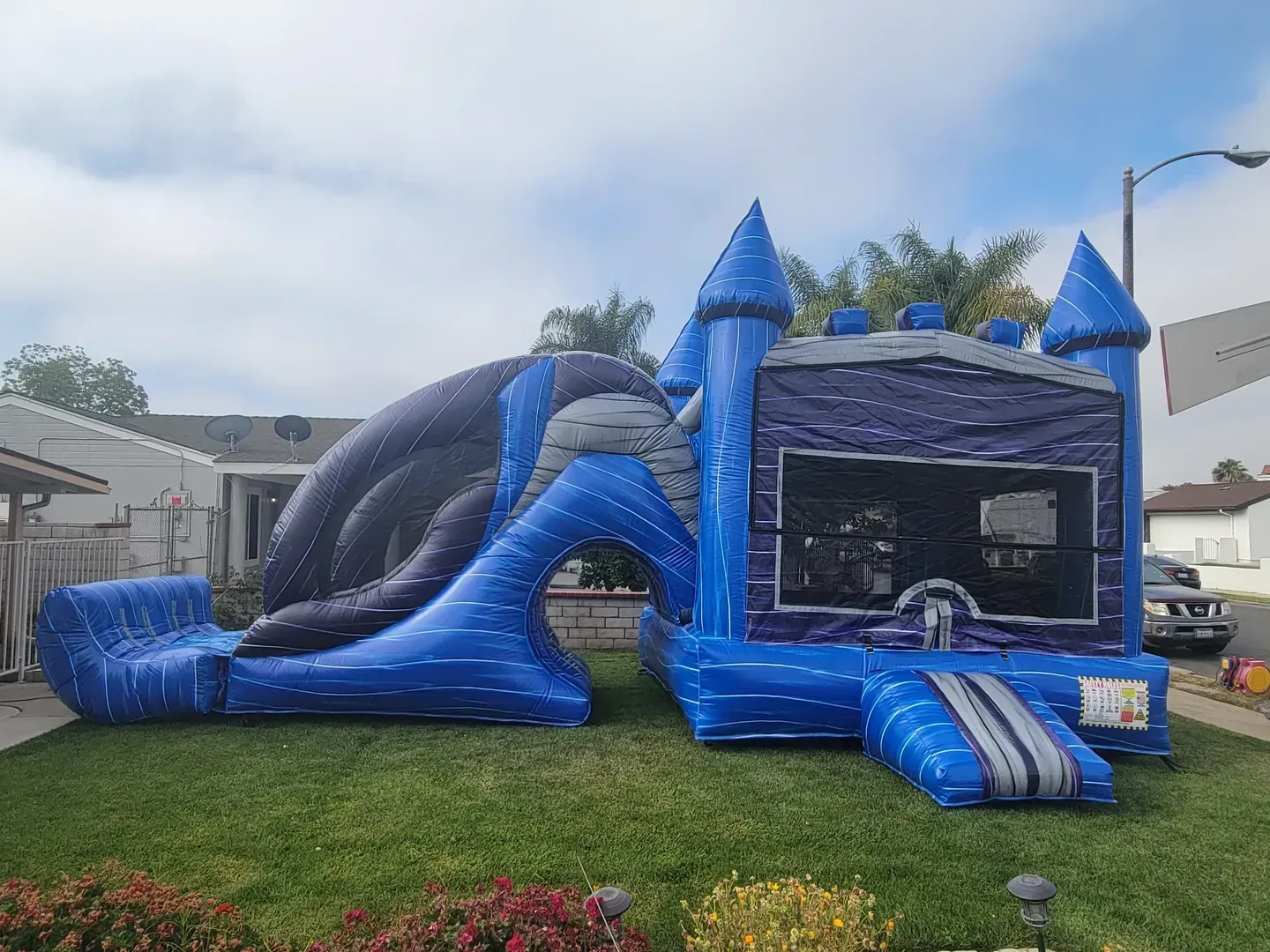 Blue inflatable castle and slide set on a grassy lawn outdoors, with a truck parked beside it.