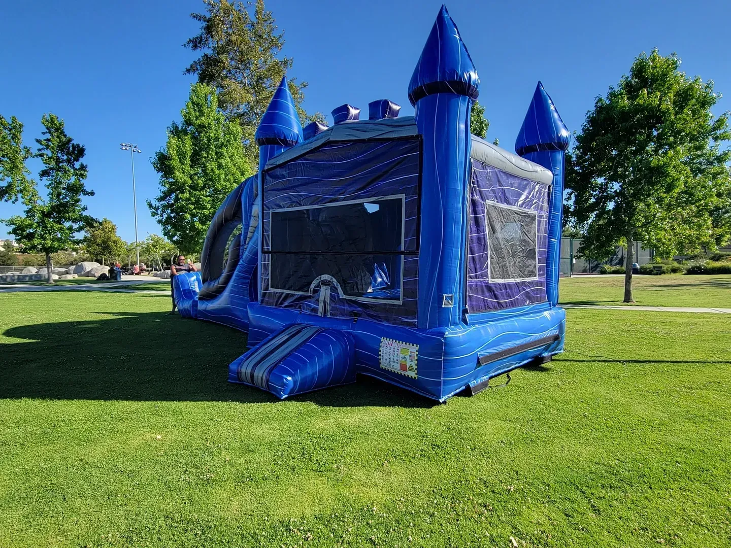 Blue inflatable bounce house with castle turrets on a grassy field under a clear sky