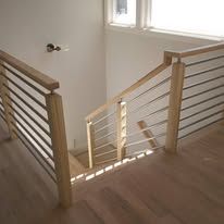 Staircase landing with light wood railings and slatted metal balusters beside a bright window