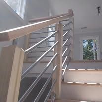 Modern indoor staircase with wood handrail, metal rails, and sunlight from a window