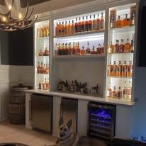 Backlit home bar with liquor bottles displayed on shelves and a wine cooler below