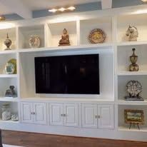 Built-in white media wall with TV, shelves of decor, and cabinets in a bright living room