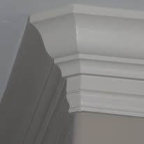 Close-up of white decorative crown molding on a gray wall, showing layered trim detail