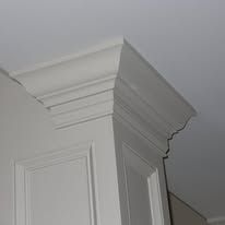 White decorative crown molding on a cabinet corner near a ceiling, with a cracked or damaged section.