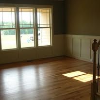 Empty living room with hardwood floors, large windows, and sunlight on the floor