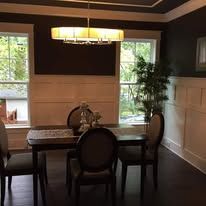 Dining room with dark wood table, upholstered chairs, and large windows with greenery outside.