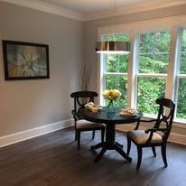 Small dining area with round table, two chairs, flowers, and large windows overlooking green trees