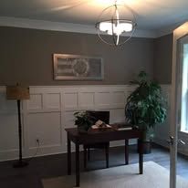 Dining room with a dark wood table, potted plant, wall art, and pendant light in a gray-and-white interior.