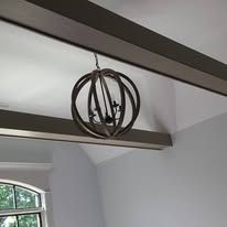 Rustic metal sphere pendant light hanging from a white vaulted ceiling with dark beams