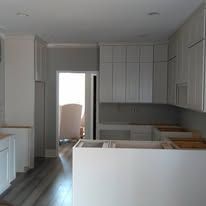 Modern white kitchen with cabinets, island, and open doorway to a lit room