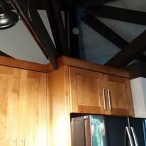 Wooden kitchen cabinets beneath dark exposed ceiling beams above a black refrigerator