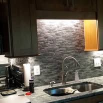 Modern kitchen sink area with dark cabinets, gray stone backsplash, and stainless steel faucet